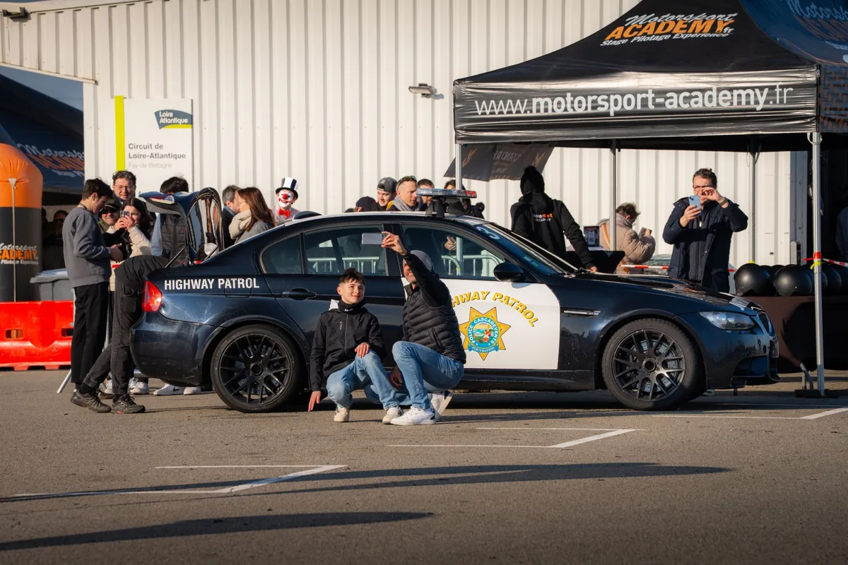 Des participants se prennent en photo devant la BMW M3, au paddock du circuit de Fay-de-Bretagne